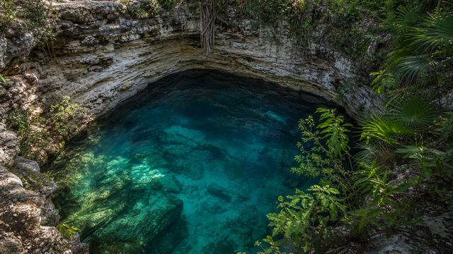 Cenote abierto con estratos de roca caliza y agua transparente, imagen conceptual